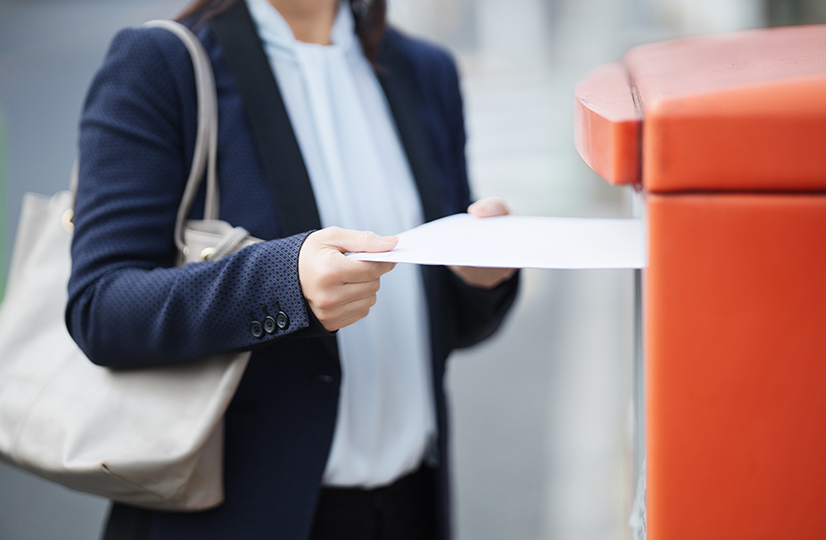 郵便ポストに書類を入れる女性